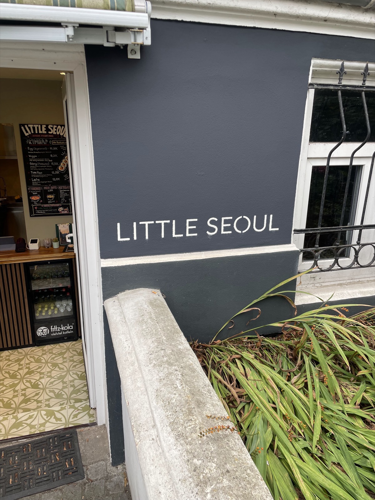 Eingang von Little Seoul mit Schriftzug an der dunklen Fassade